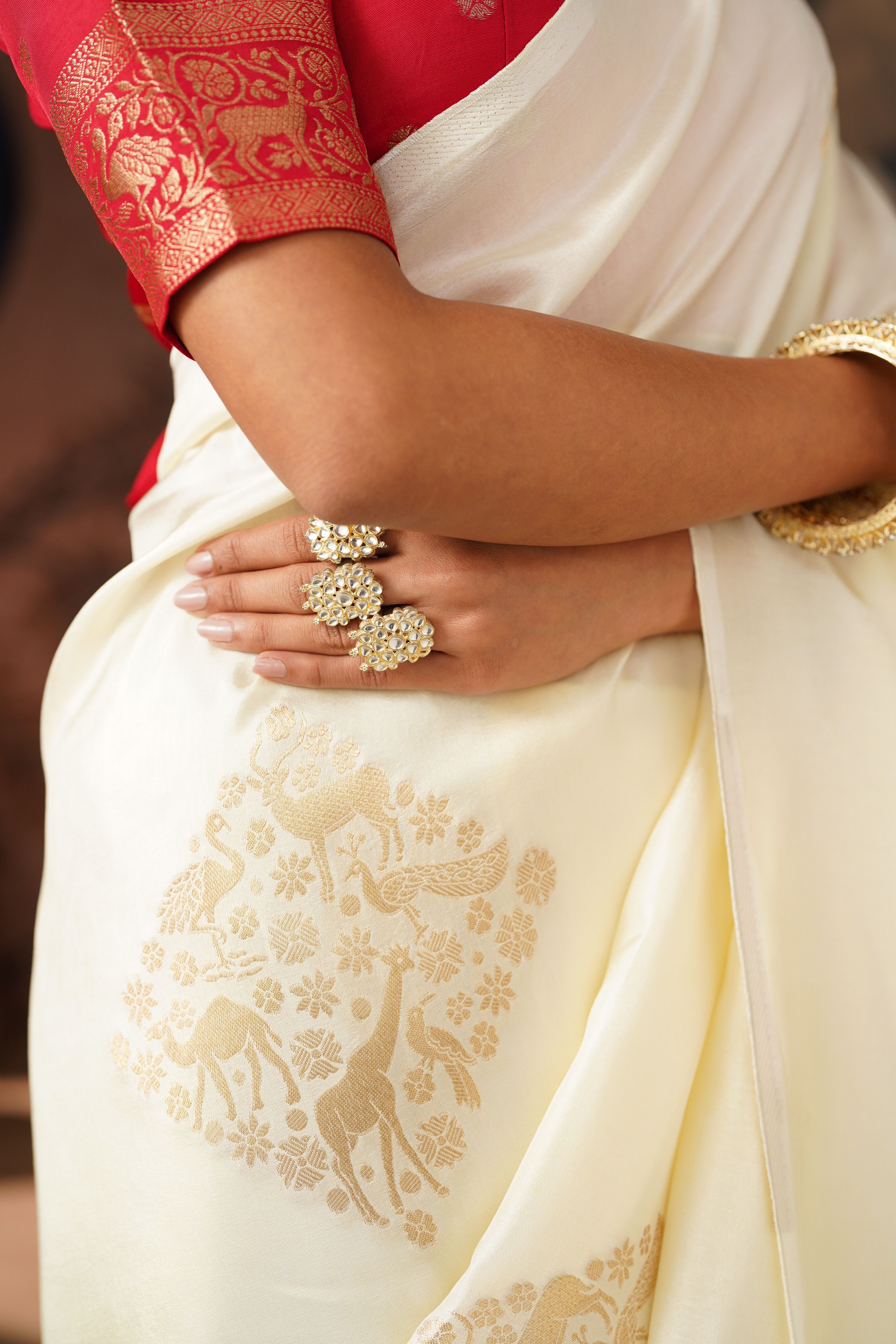 Model wearing a gold saree with teal motifs beneath garden arches